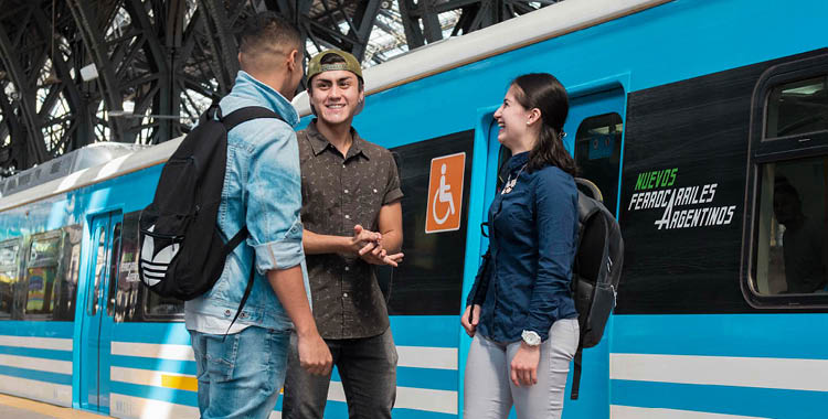 Three students chat next to a blue train in Buenos Aires, Argentina.