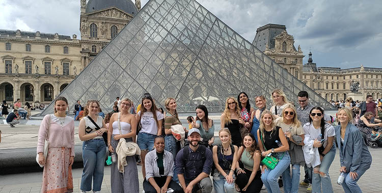 A group of students pose in front of the glass pyramid of the Musee du Louvre in Paris, France.