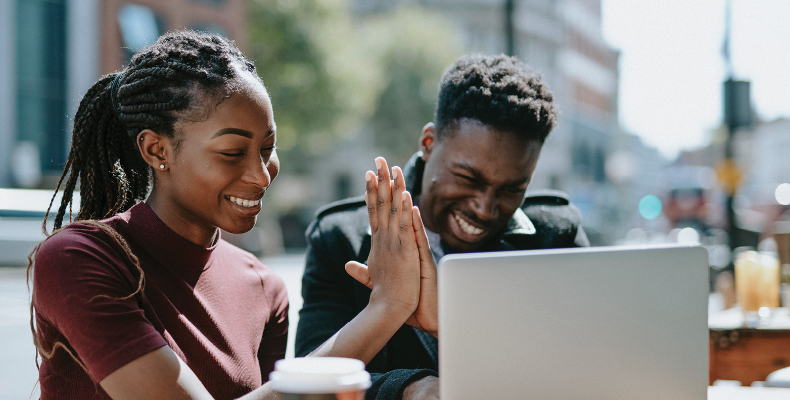 Students high five while working on a laptop in a public space.